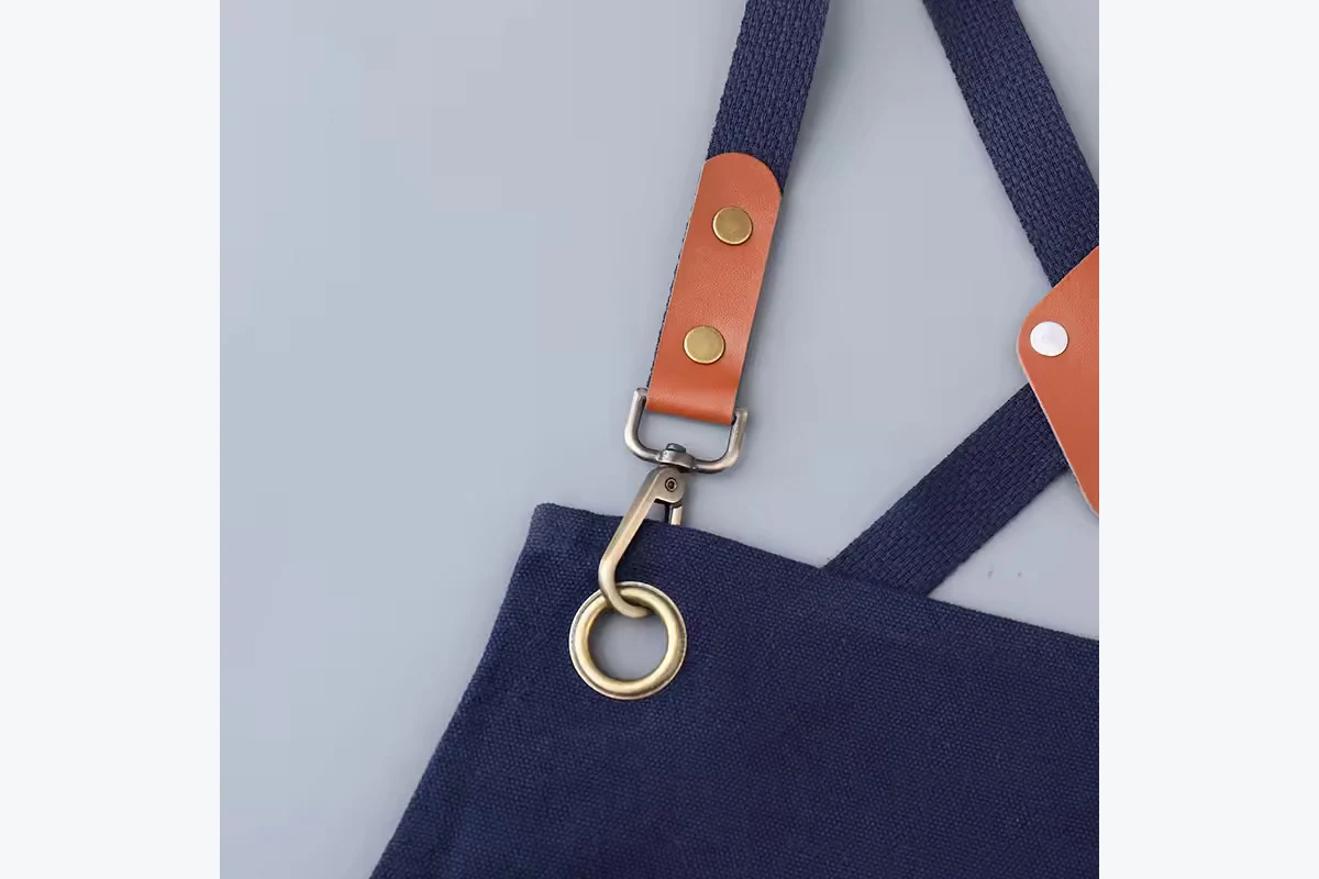 Brown strap tabs, metal clips, and a ring on a navy apron.