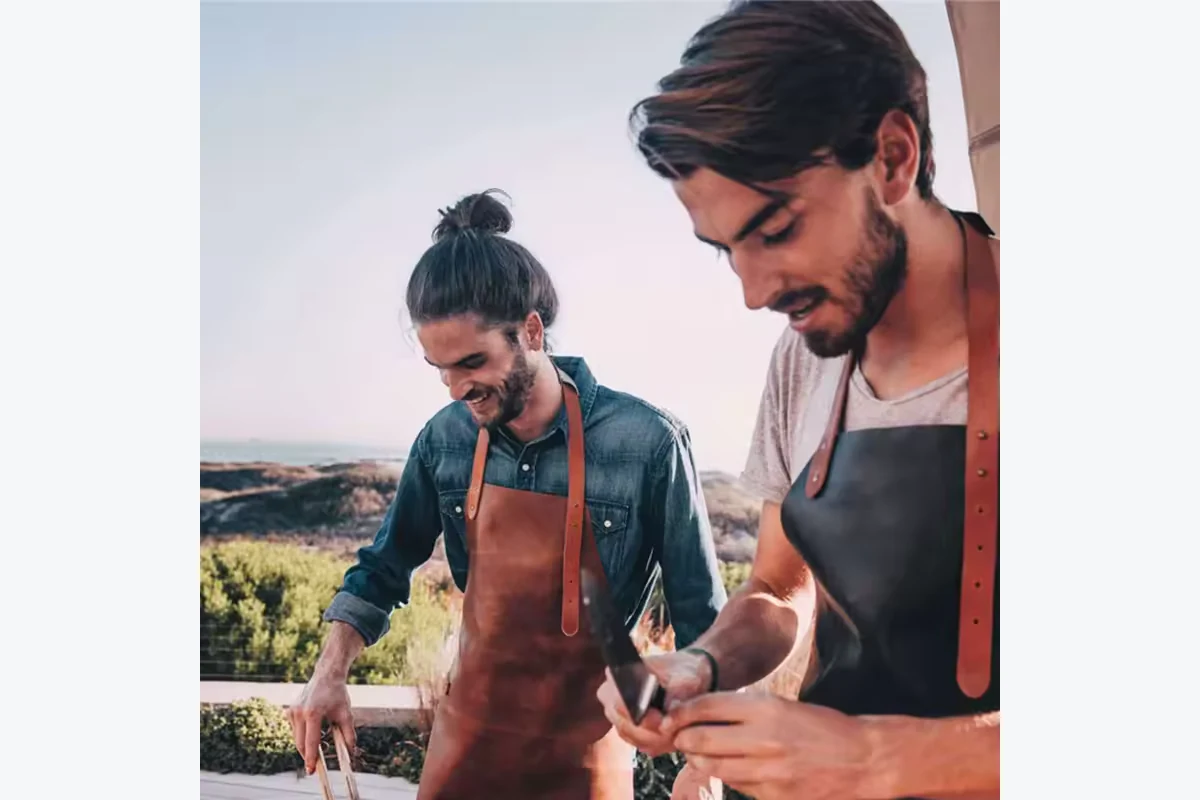 Two people wearing brown and black aprons while cooking outdoors.
