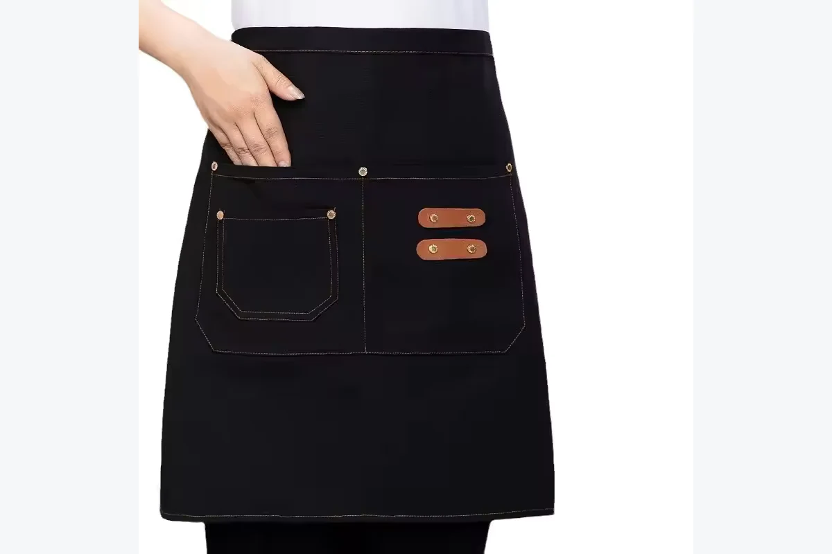 Black waist apron with front pockets and brown fastening tabs.