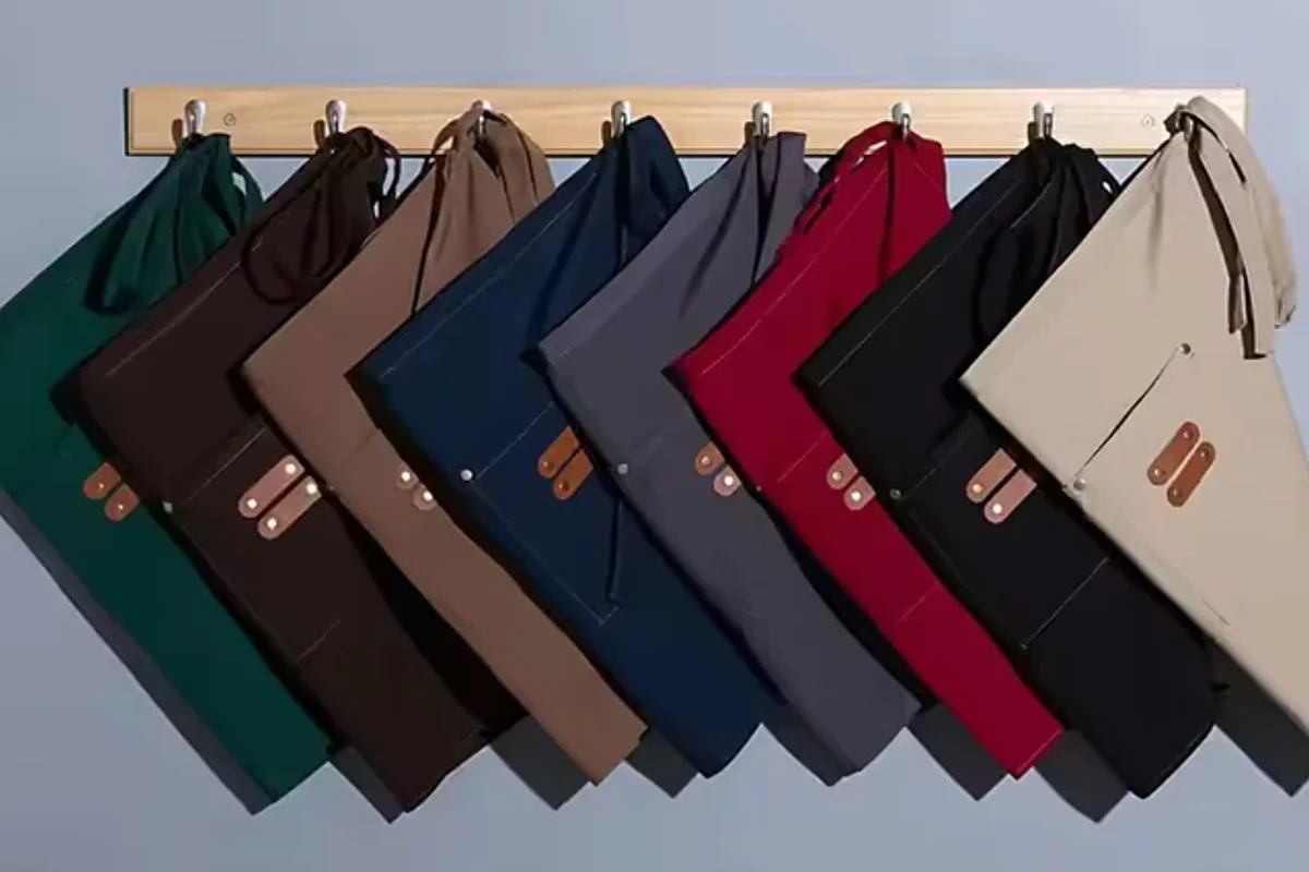 Waist aprons hanging in several dark and neutral colors.